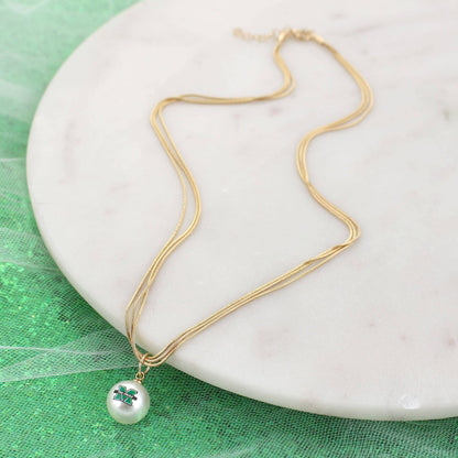 Gold necklace with a pearl pendant on a white plate against a green background