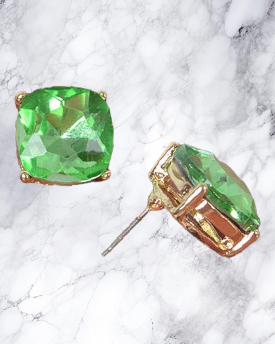 the green square stud earrings lie on a marble surface