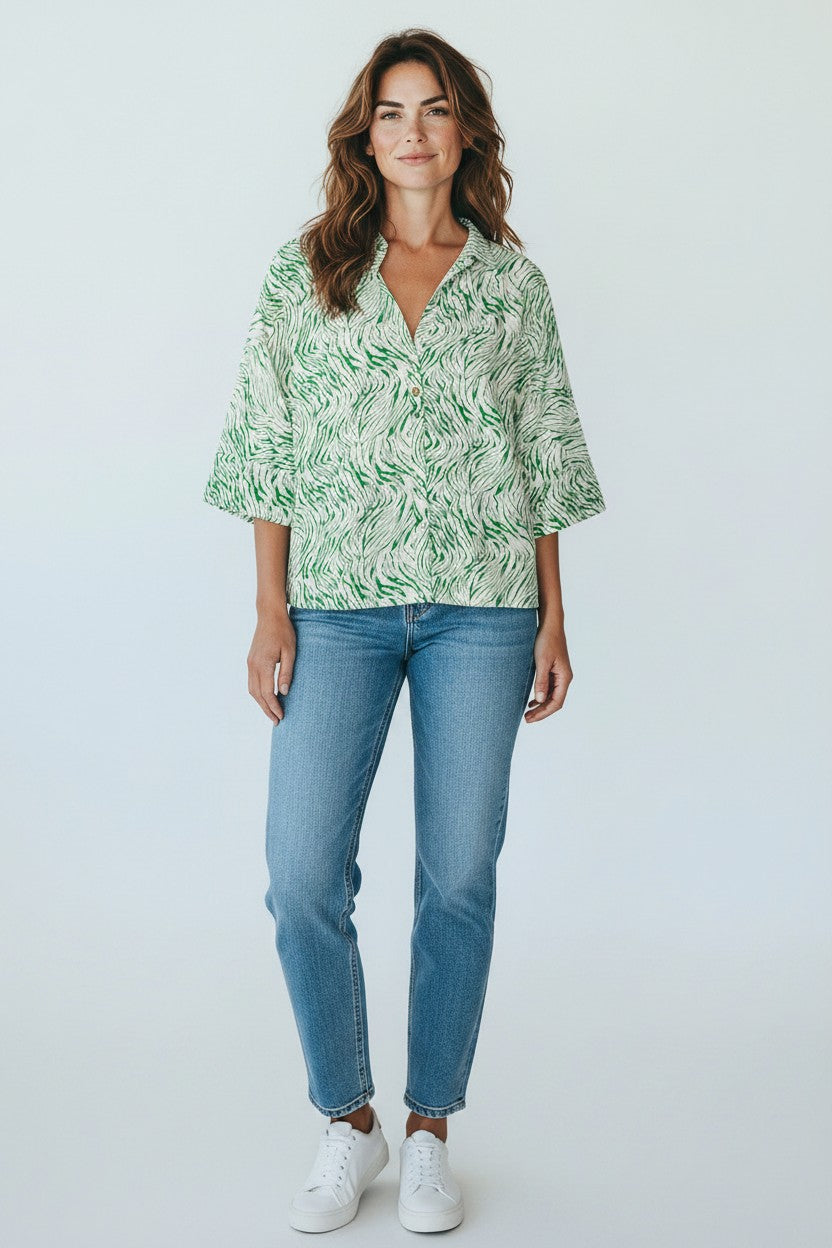 Woman wearing a green patterned blouse and blue jeans against a white background