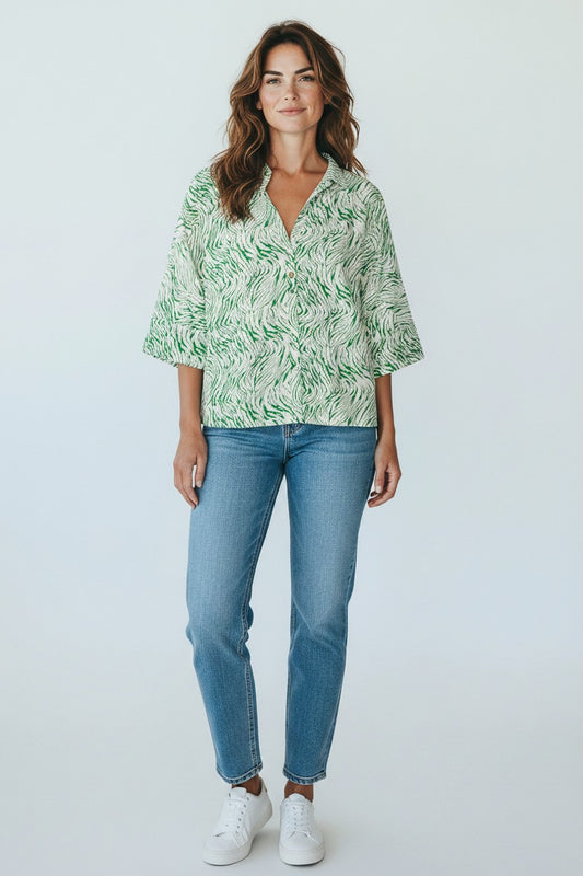 Woman wearing a green patterned blouse and blue jeans against a white background