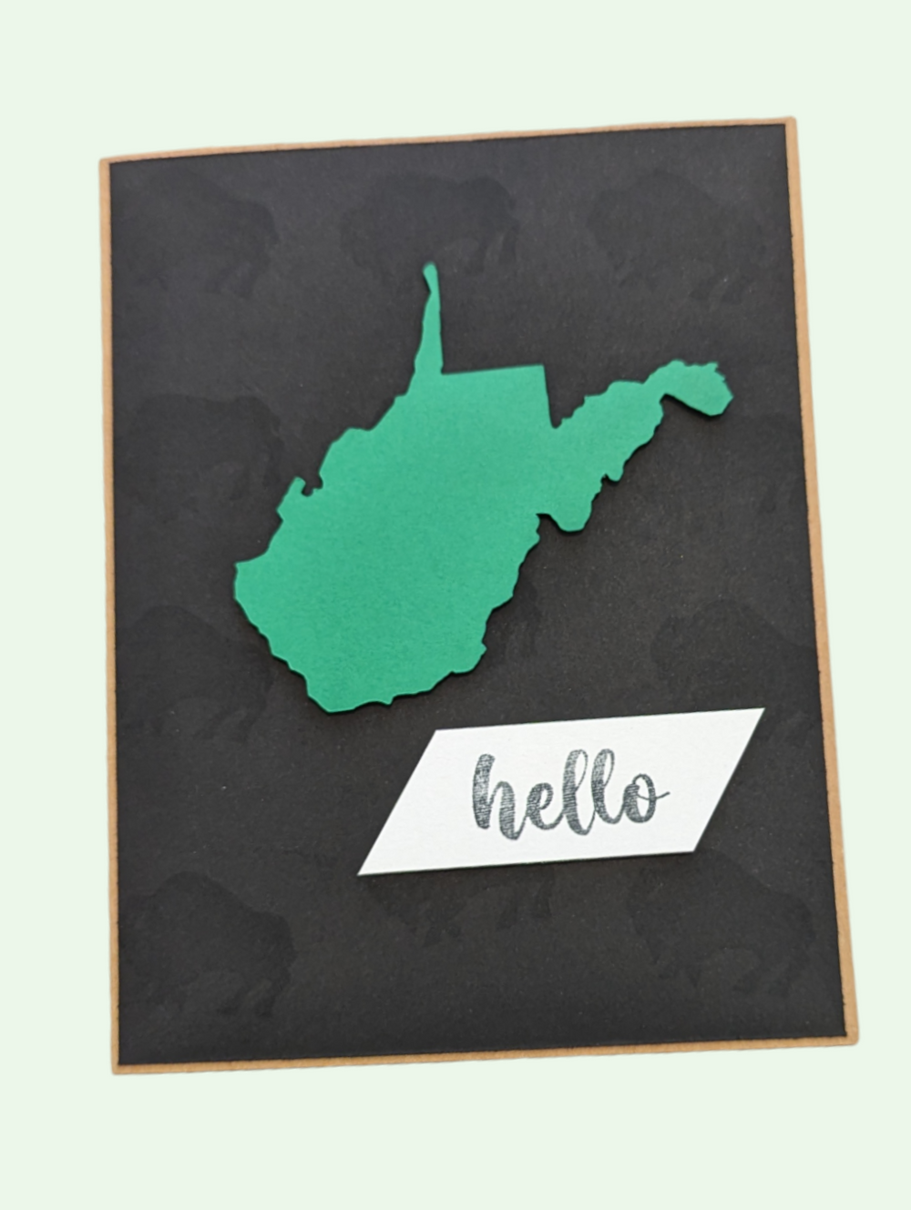 the green hello card with the outline of wv in green and hello on a white plate on a black background