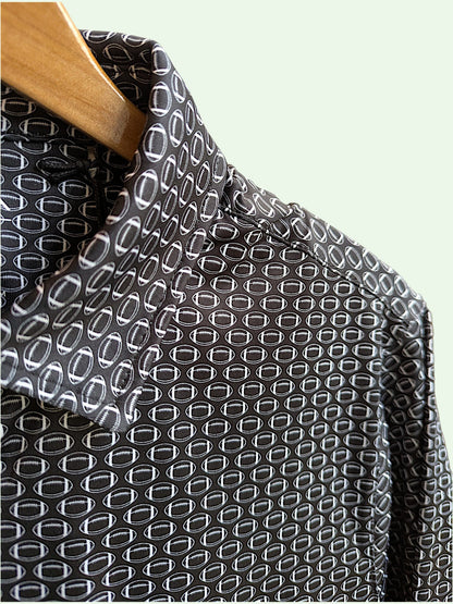 A close-up of a black football patterned shirt with a white geometric repeating pattern, hanging on a wooden hanger against a pale mint green background.