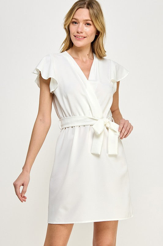 a blonde model poses in the ivory faux wrap dress, accenting the waistband with one hand