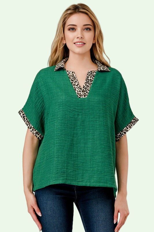 Woman wearing a green top with leopard print trim on a plain background
