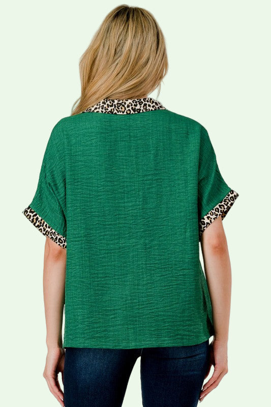 Green top with leopard print cuffs and collar worn by a person on a plain background