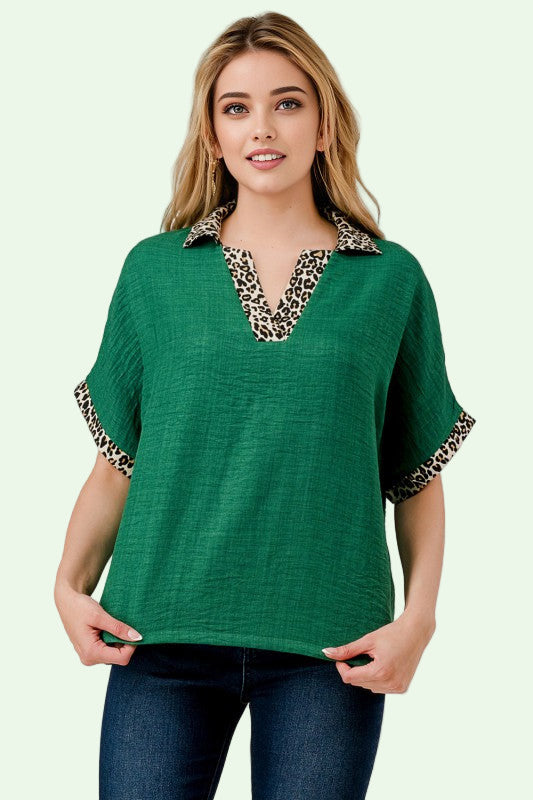 Woman wearing a green top with leopard print trim on a plain background
