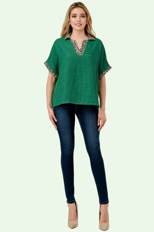 Woman wearing a green top with decorative trim and blue jeans on a white background