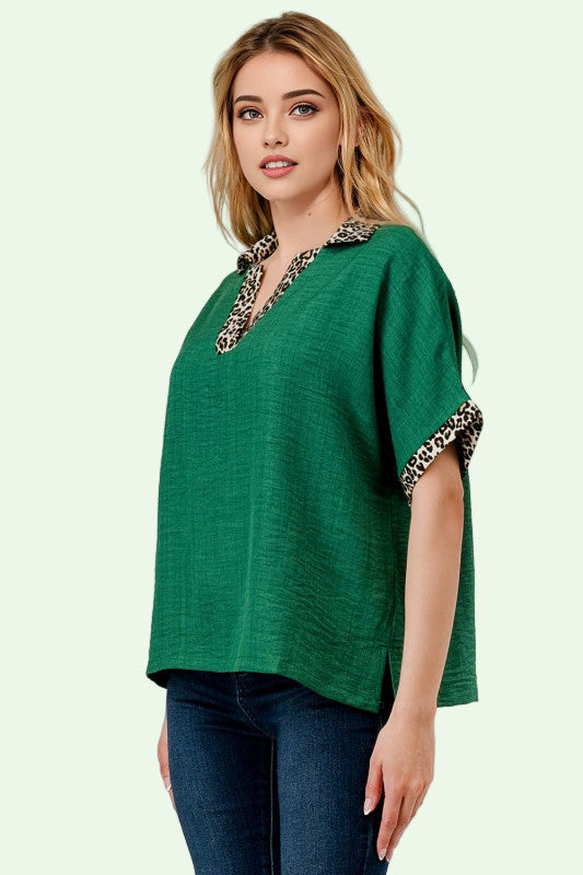 Woman wearing a green top with leopard print details on a plain background