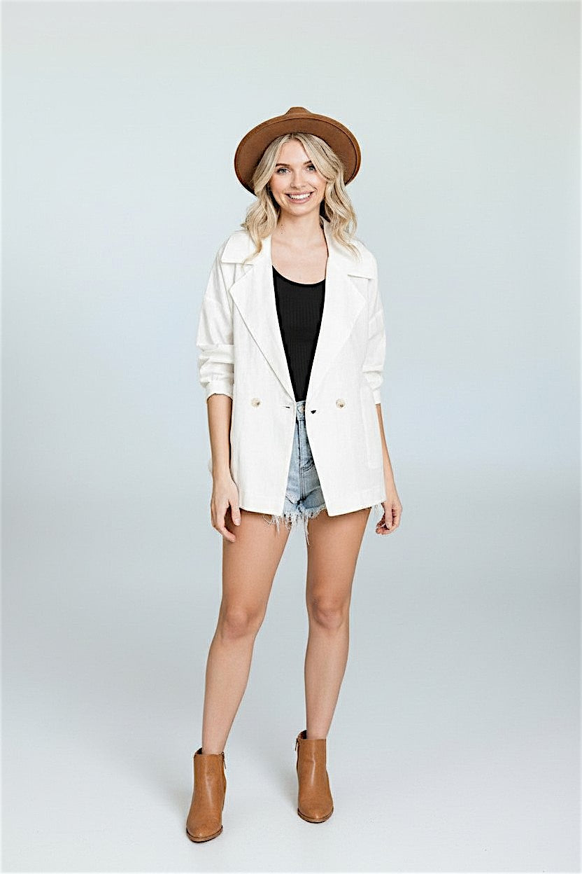 Woman wearing a white jacket, black top, denim shorts, and brown boots on a white background