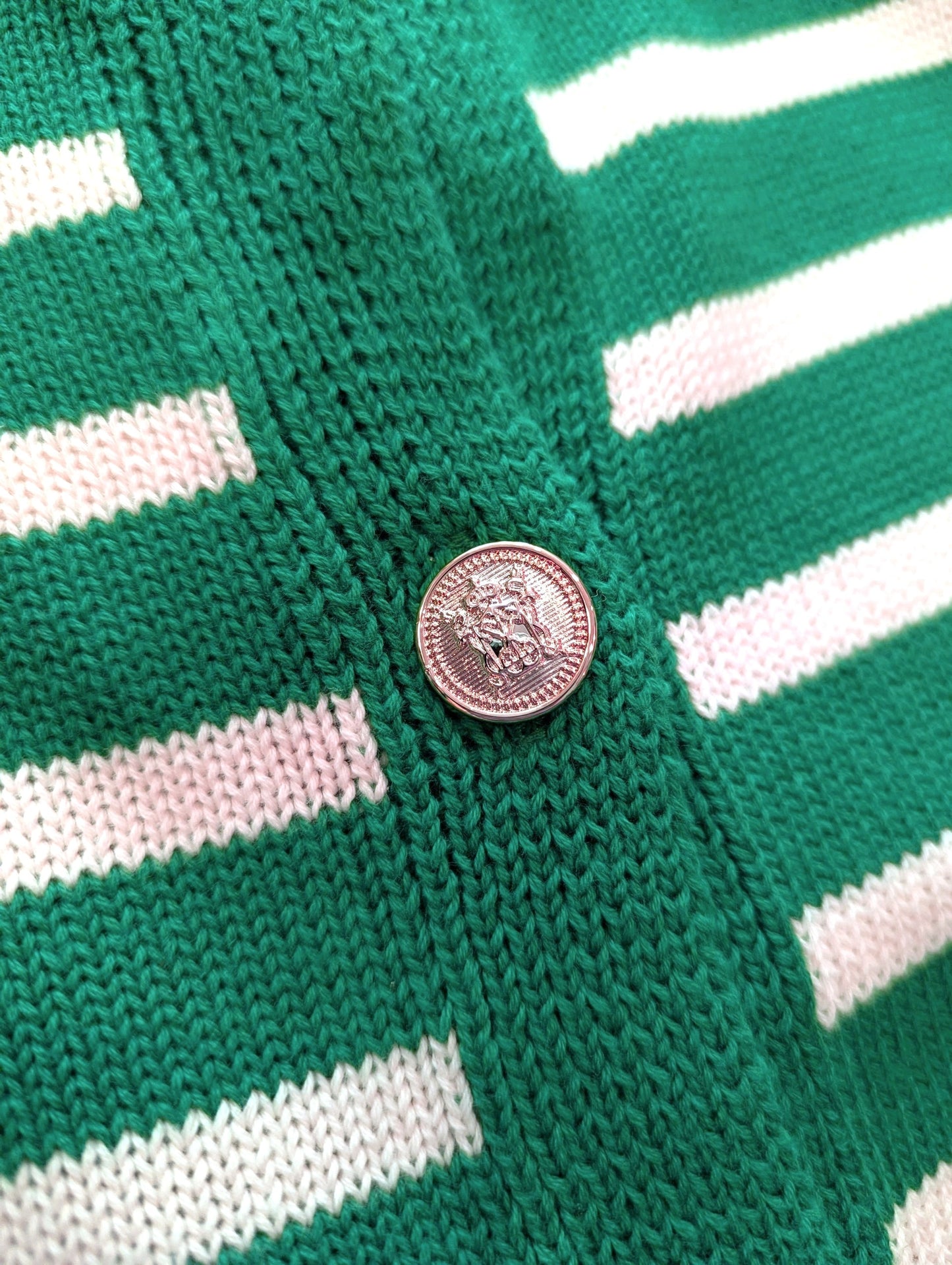 Close-up of a green and white striped knit garment with a round metallic button.