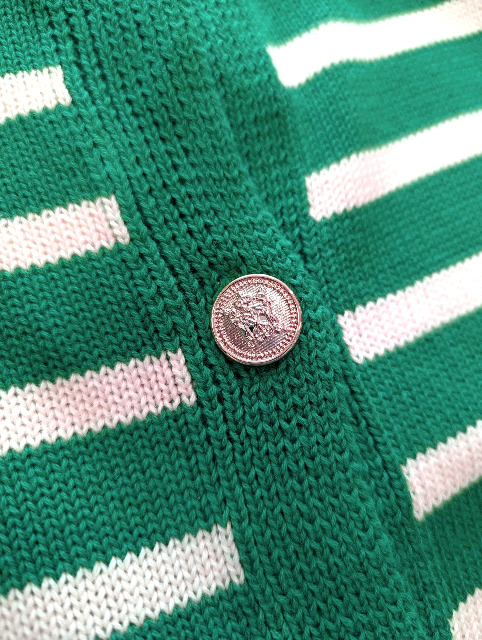 Close-up of a green and white striped knit garment with a round metallic button.