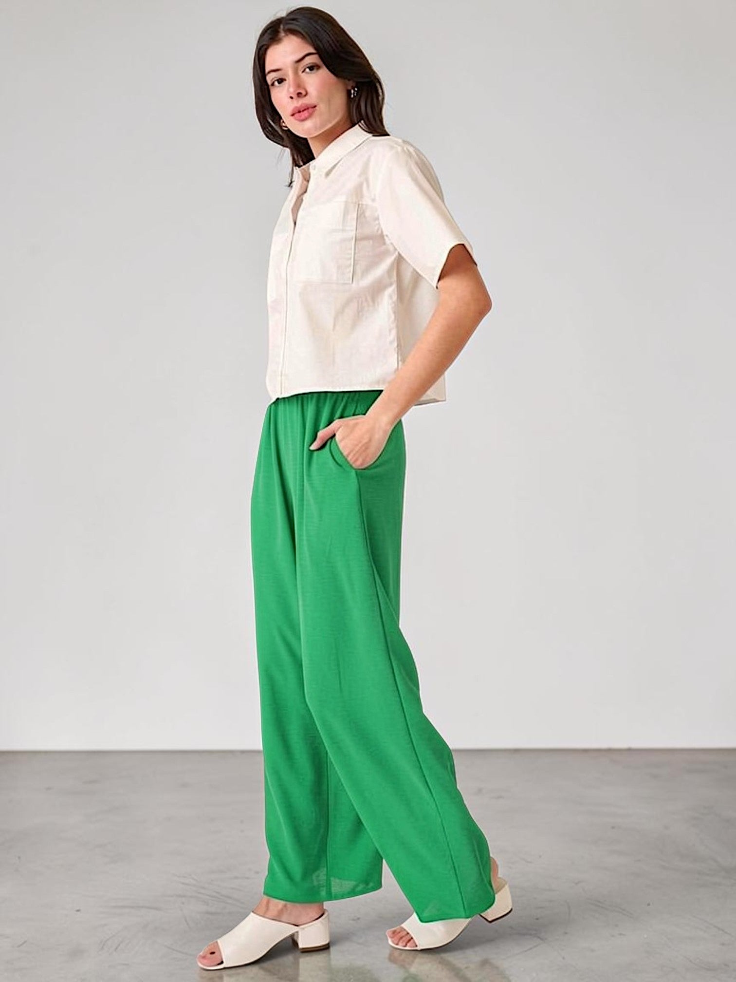 Woman wearing a white blouse and green pants against a plain background