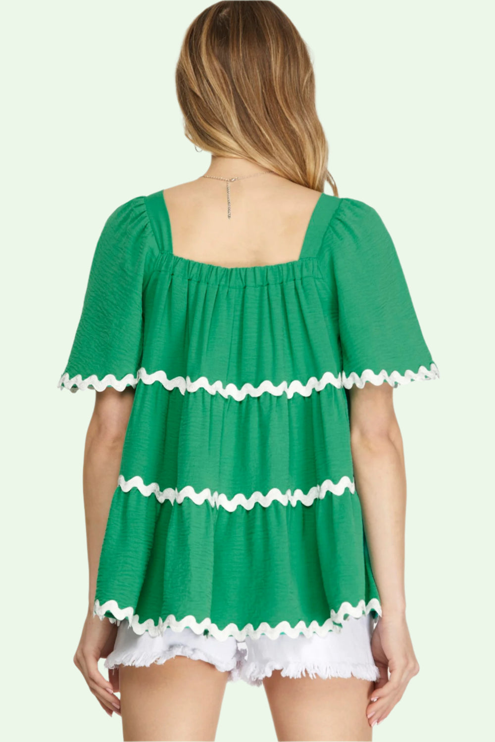 Green top with white ruffle details on a plain background