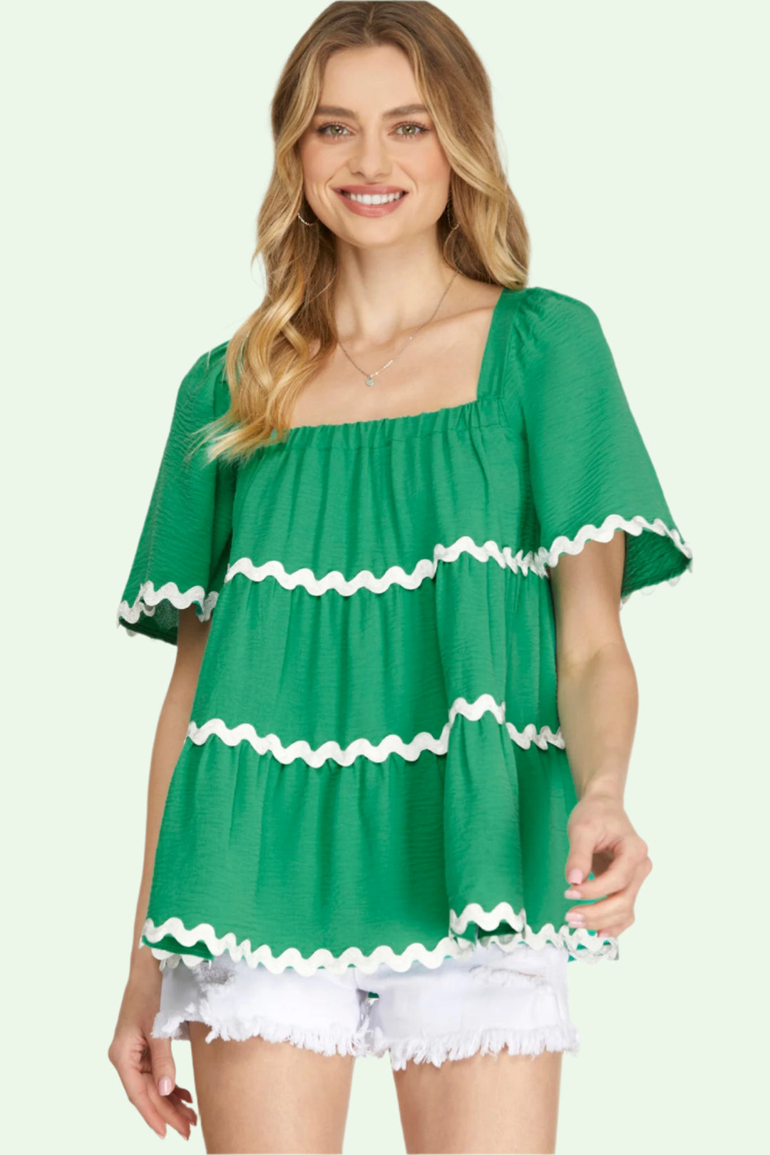 Woman wearing a green blouse with white ruffled trim on a white background