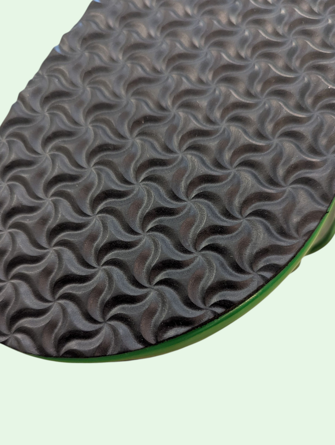Close-up of a textured shoe sole with wavy pattern on a light green background