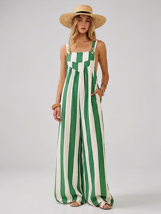 A woman modeling a green and off-white vertically striped wide-leg jumpsuit with a straw sun hat against a light gray studio background.