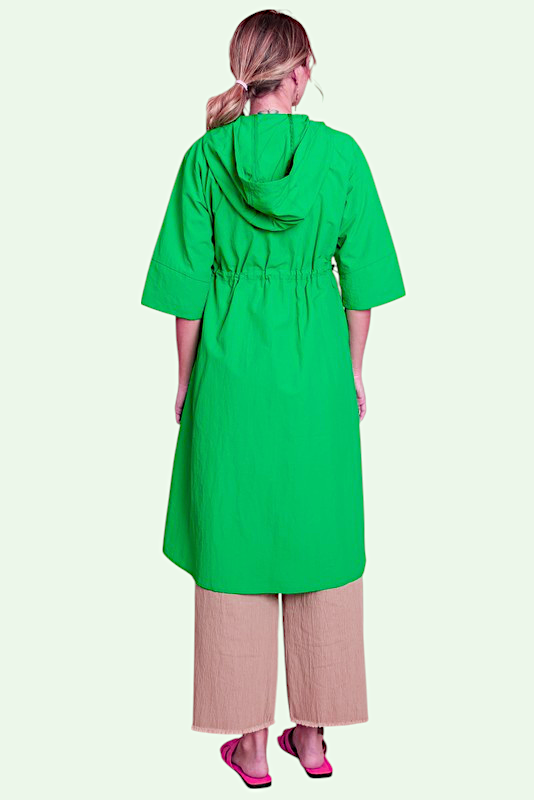 Person wearing a green hooded dress with beige pants on a white background