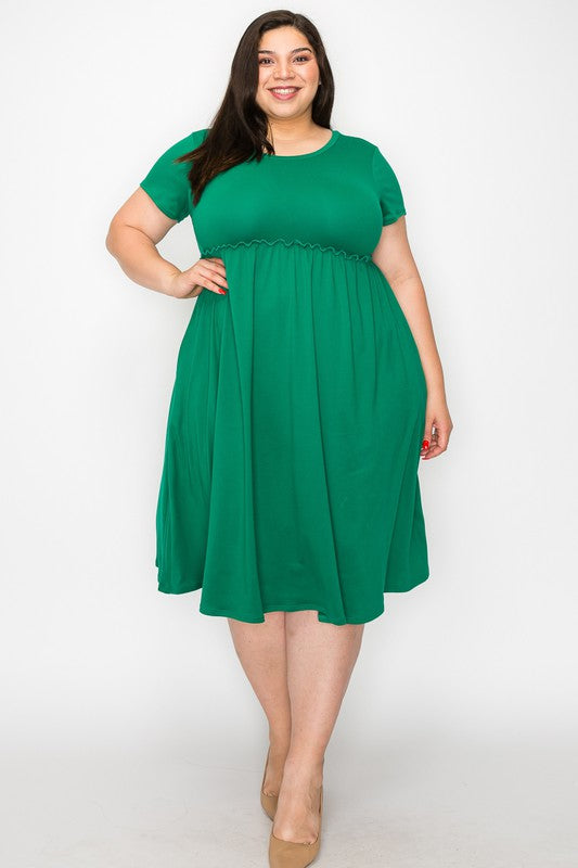 a dark haired model stands in a full-length shot in a green dress facing the camera