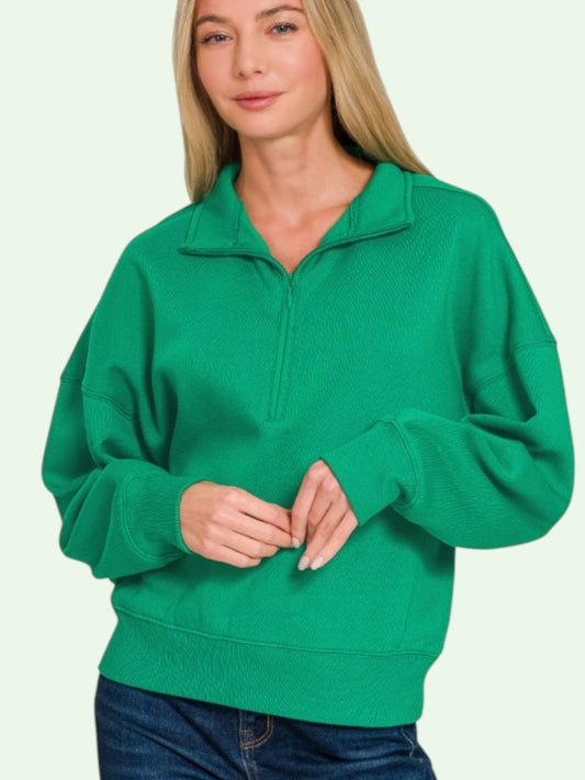 Woman wearing a green pullover with a half zip on a light green background