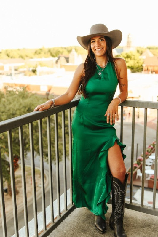 Woman in a green dress and cowboy boots on a balcony with a scenic background