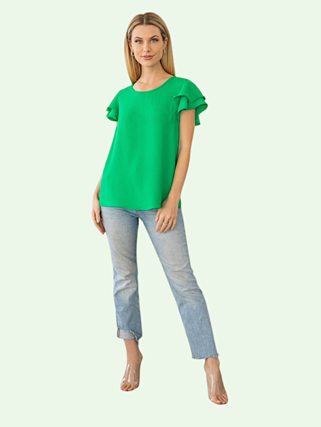 Woman wearing a green blouse with ruffled sleeves and light blue jeans on a white background