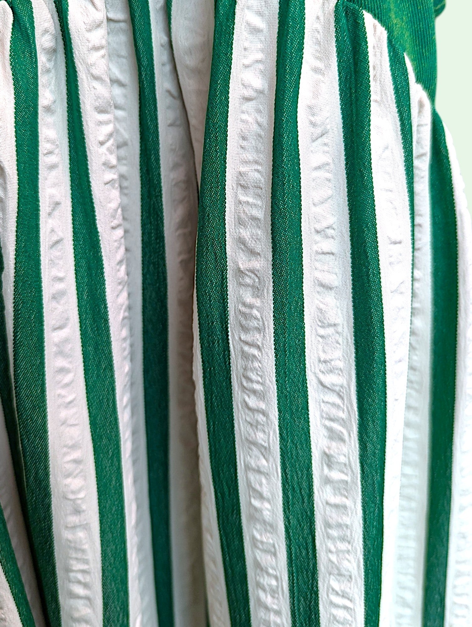 A close-up of a green and white vertically striped fabric with textured, gathered pleats.