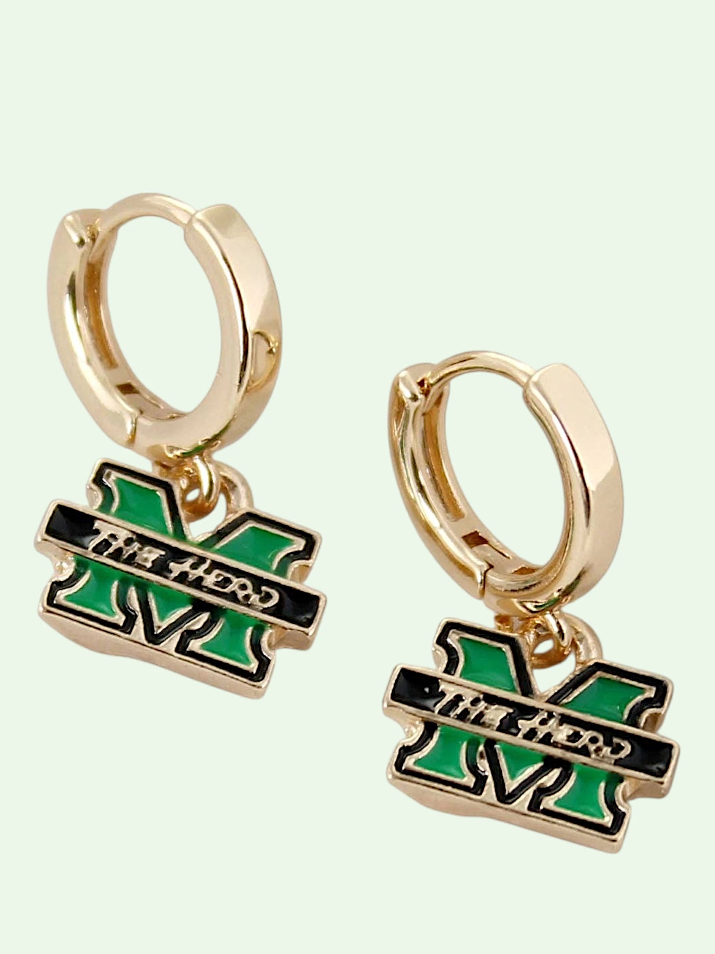 A pair of gold huggie hoop earrings with dangling charms shaped like the letter 'M' in a MARSHALL color scheme of green and black, featuring the text 'The Herd' across a black bar.