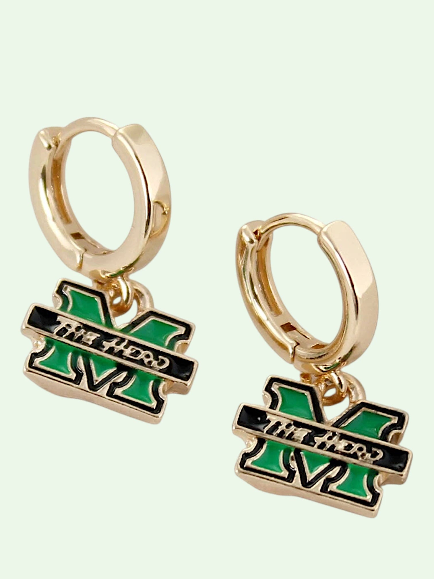 A pair of gold huggie hoop earrings with dangling charms shaped like the letter 'M' in a MARSHALL color scheme of green and black, featuring the text 'The Herd' across a black bar.