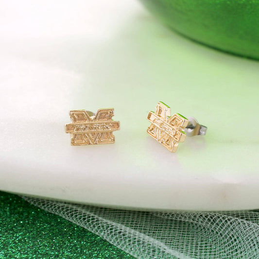 Gold geometric earrings on a white surface with a green fabric background