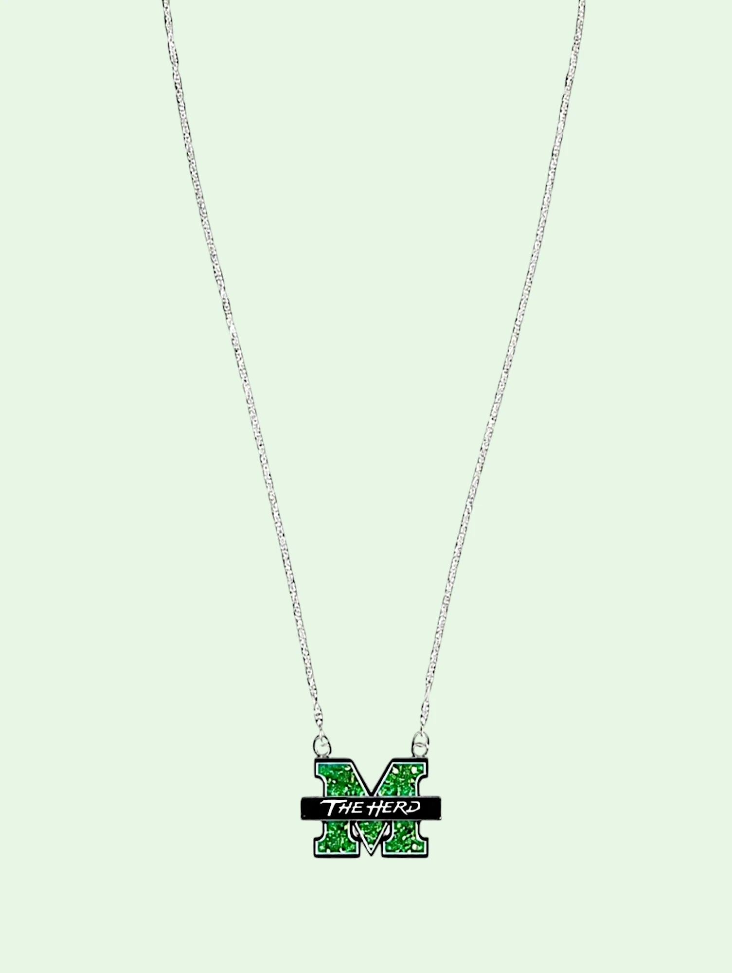 A silver chain necklace featuring a green and black enamel 'M' pendant with the text 'THE HERD' on a light mint green background.
