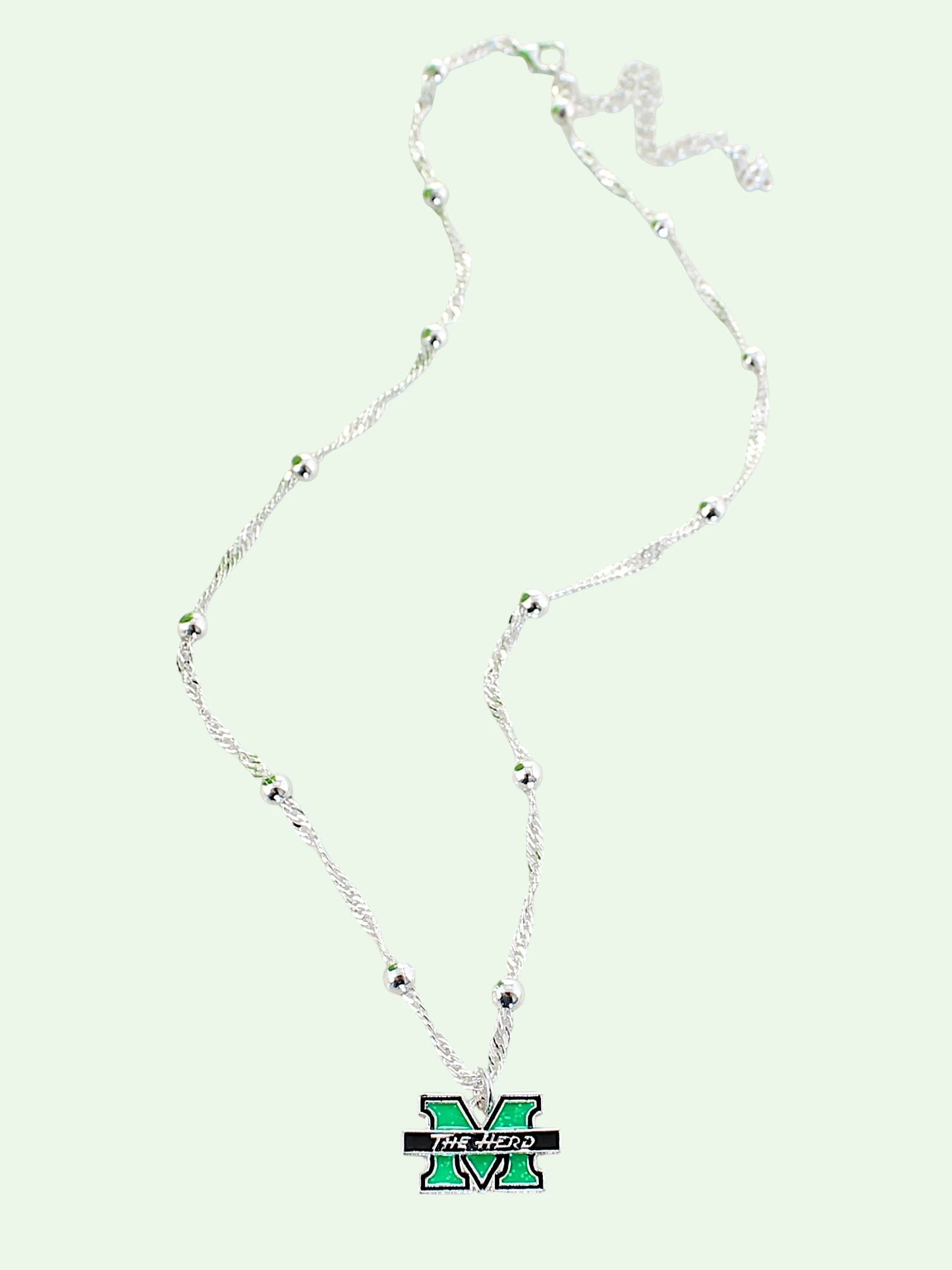 A silver beaded necklace featuring a green and black Michigan 'M' logo pendant, displayed on a pale mint green background.