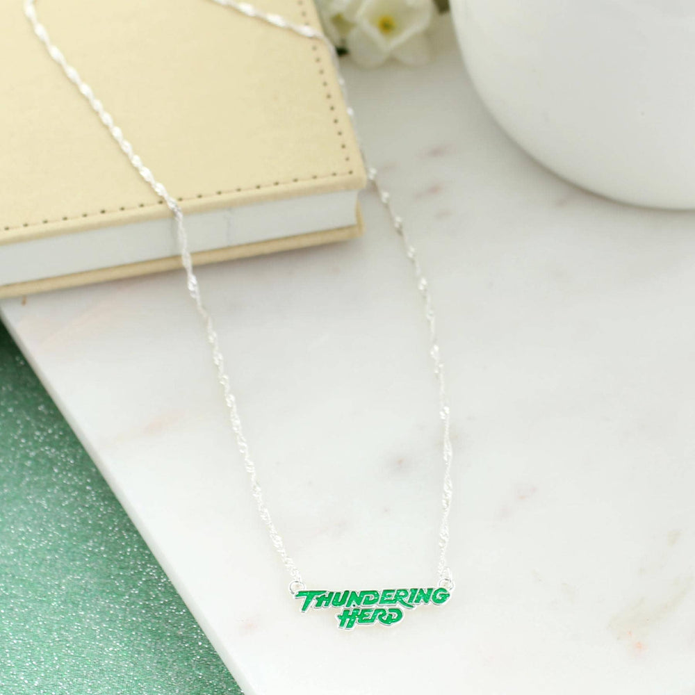 Silver necklace on a marble surface with a notebook and small plant, branded 'Thundering Herd'.