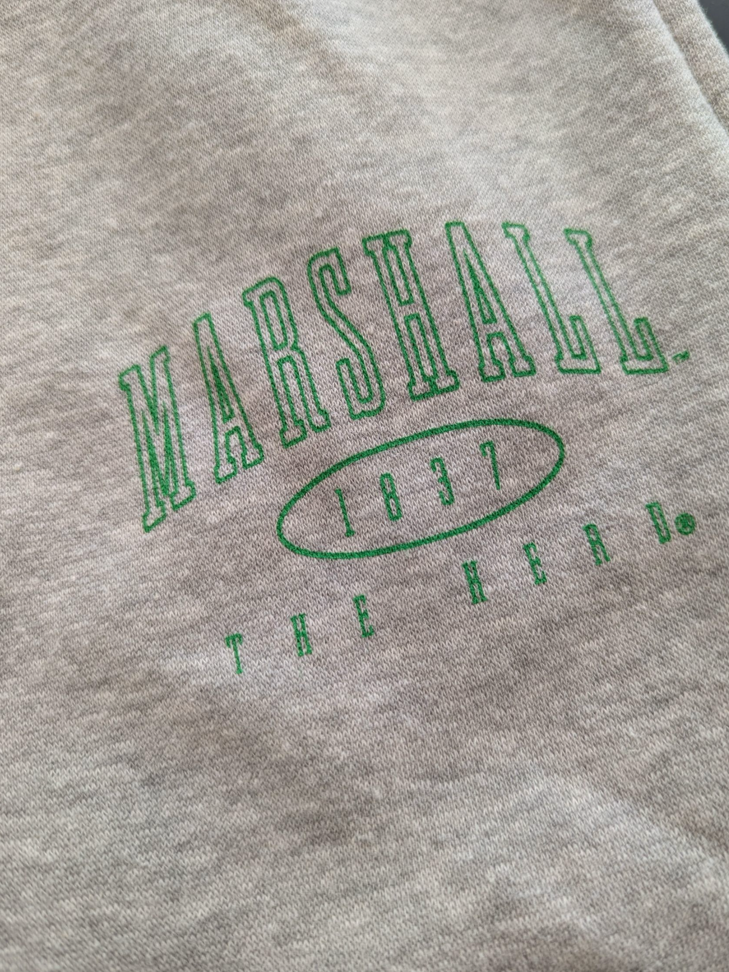 Gray sweatshirt with green 'Marshall 1837 The Herd' text on a close-up view