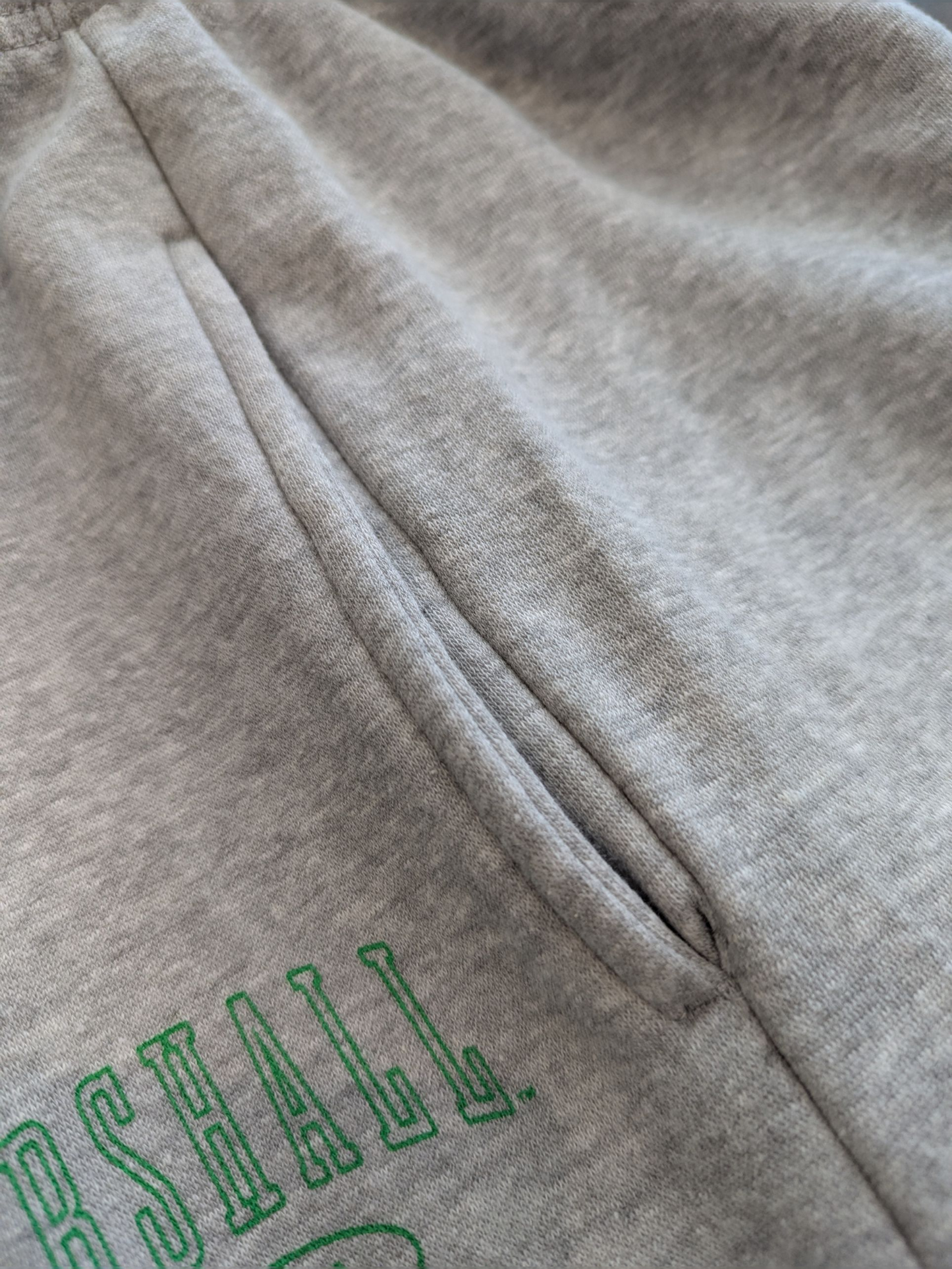 Gray sweatpants with green text on a close-up view of the side pockets