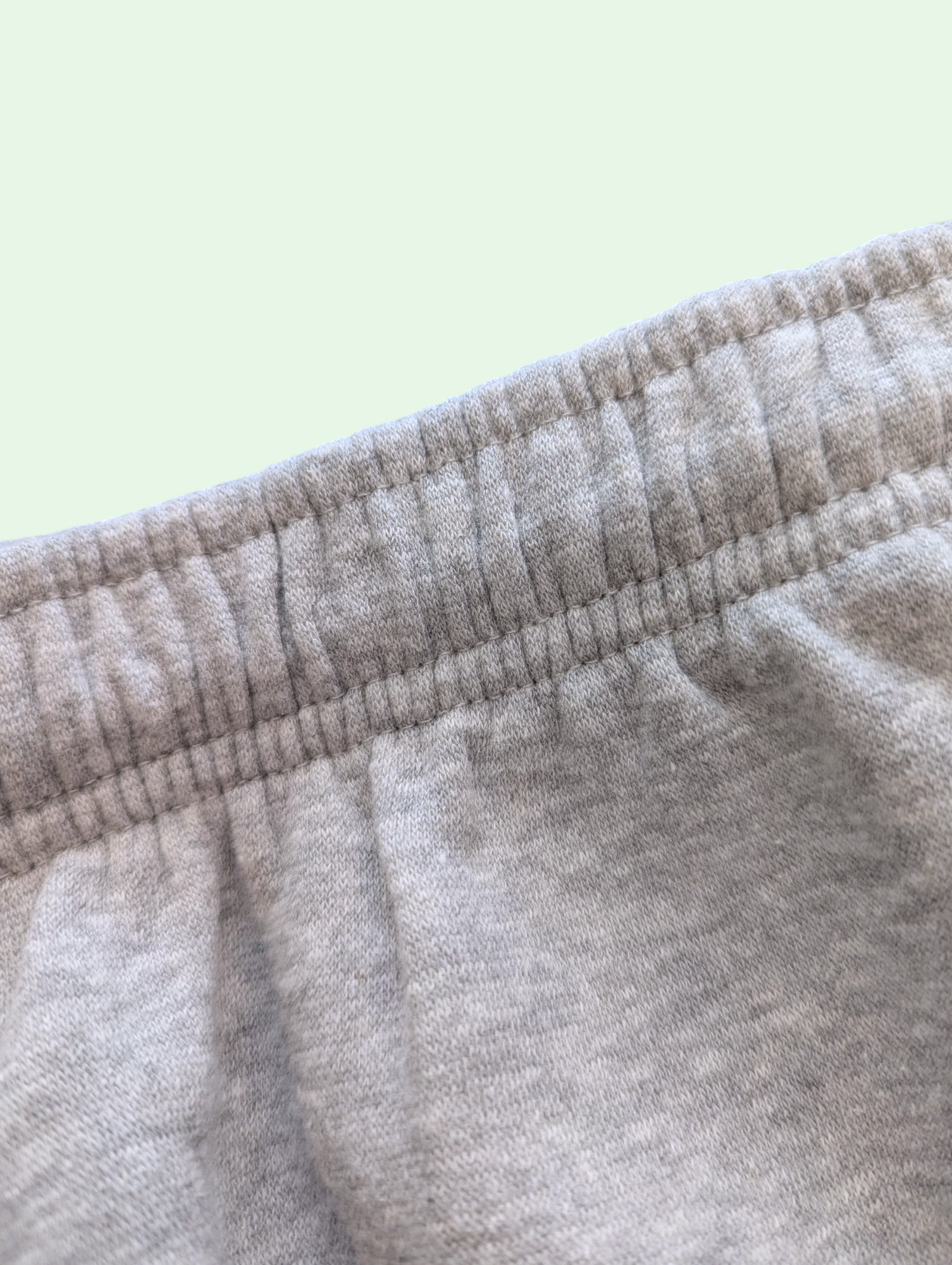 Close-up of the waist of gray sweatpants with a light green background