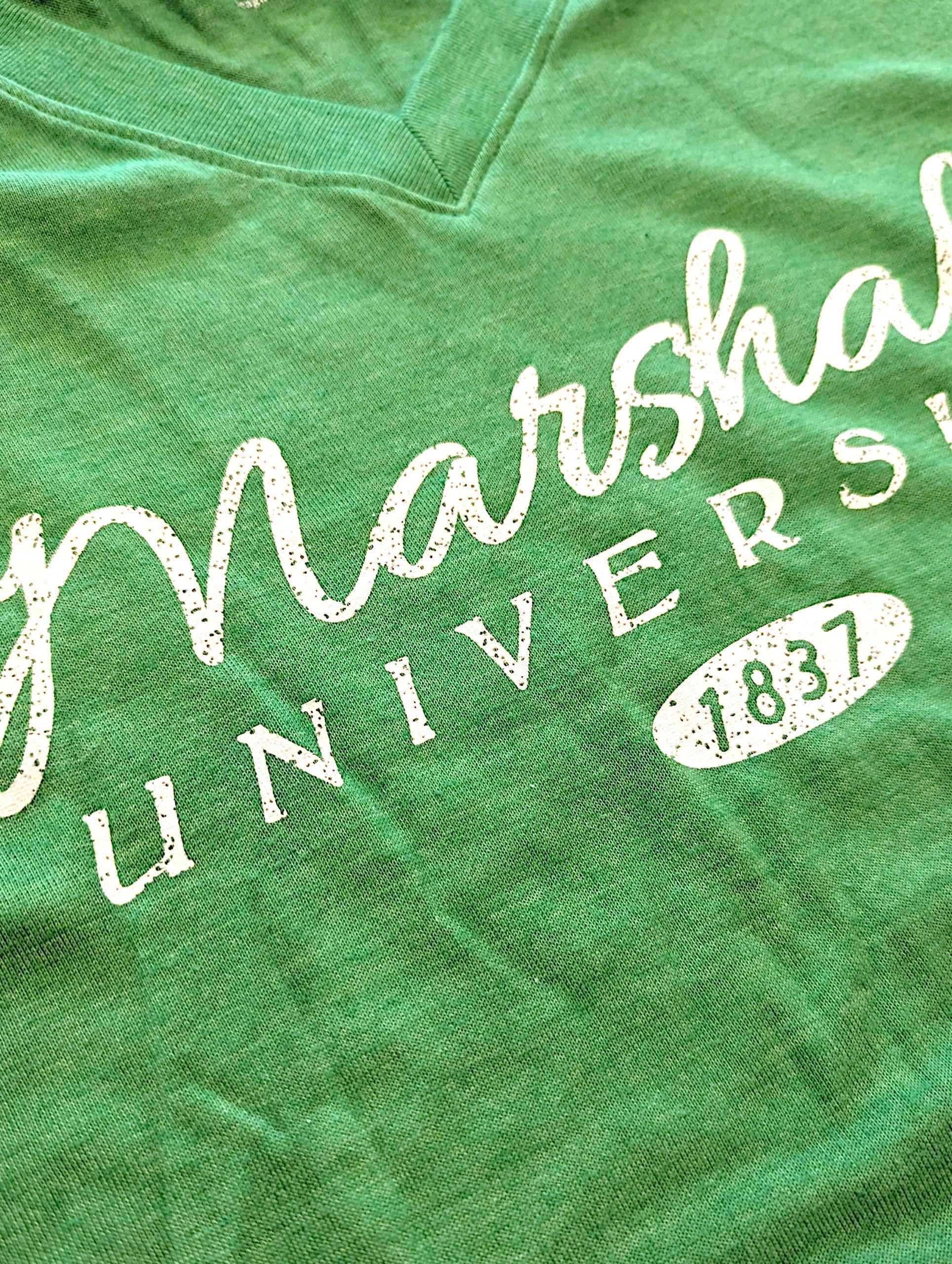 Close-up of a green heather V-neck t-shirt featuring a distressed white graphic print that reads 'Marshall University 1837'.