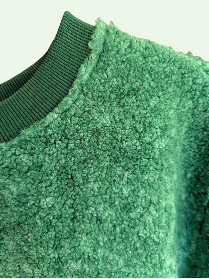 Close-up of a green fleece or sherpa sweater with a ribbed knit collar, showing the textured fabric and neckline detail.