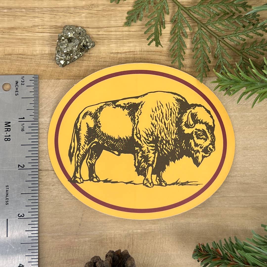 Round yellow sticker with a black buffalo design on a wooden surface with a ruler for scale.