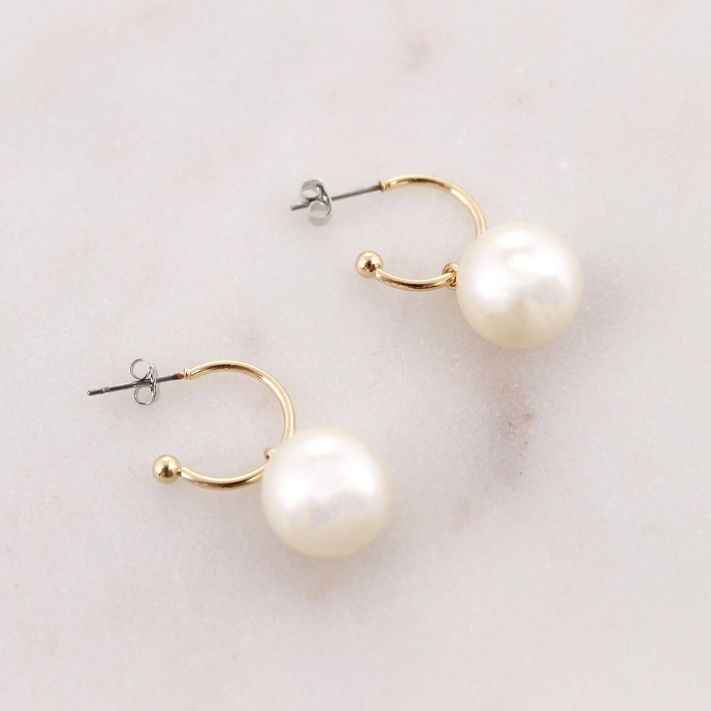 Pair of pearl earrings with gold hoops on a light background