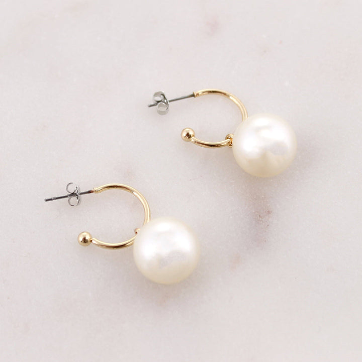 Pair of pearl earrings with gold hoops on a light background