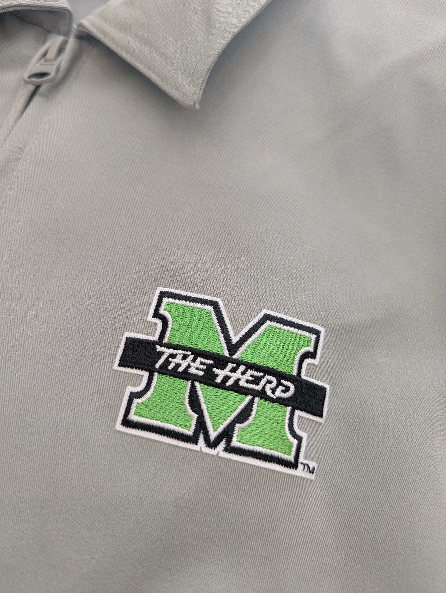 Gray jacket with a green and black logo on the chest, close up detail 
