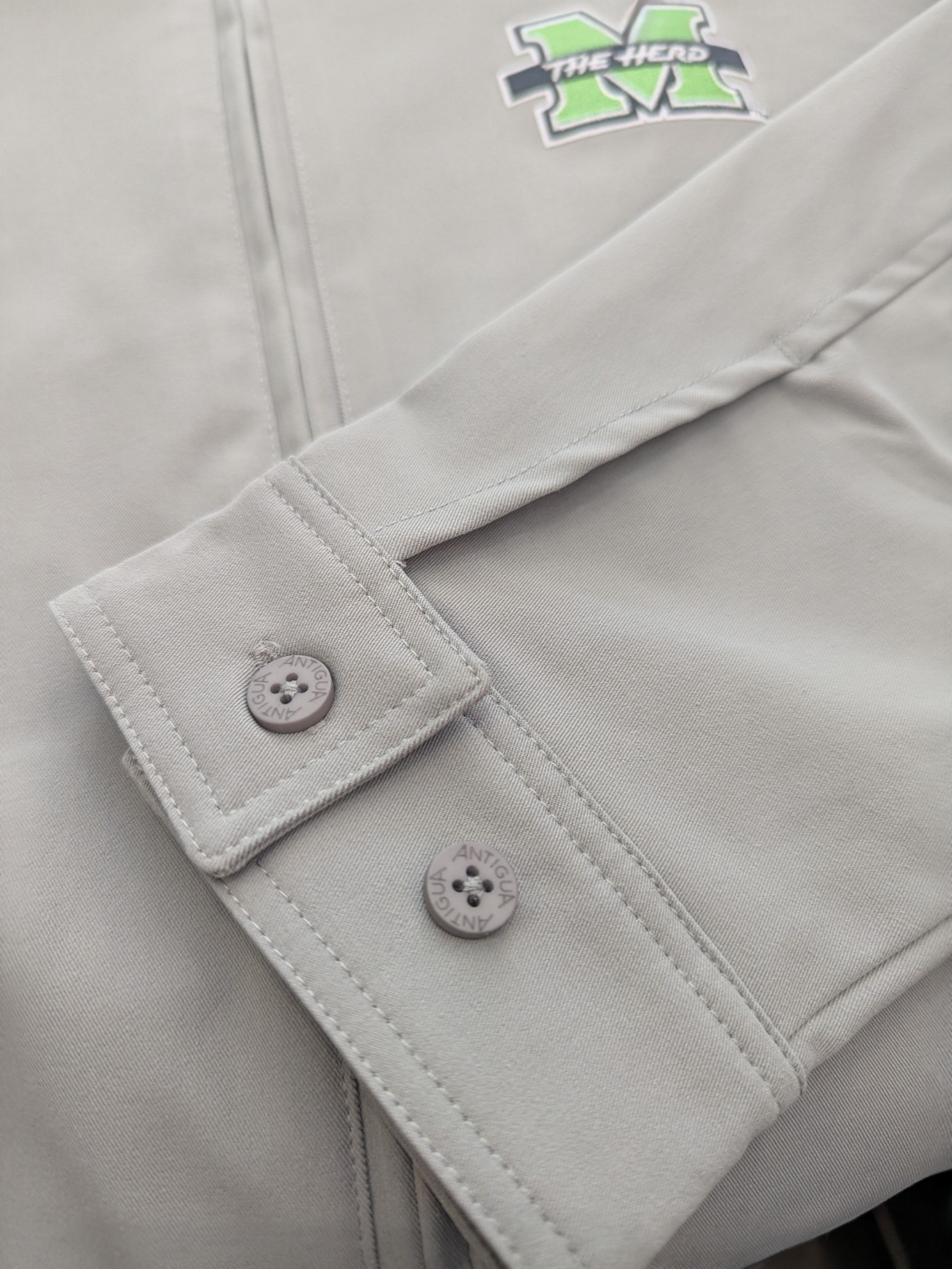 Close-up of a gray jacket sleeve with buttons and a logo on a light gray background
