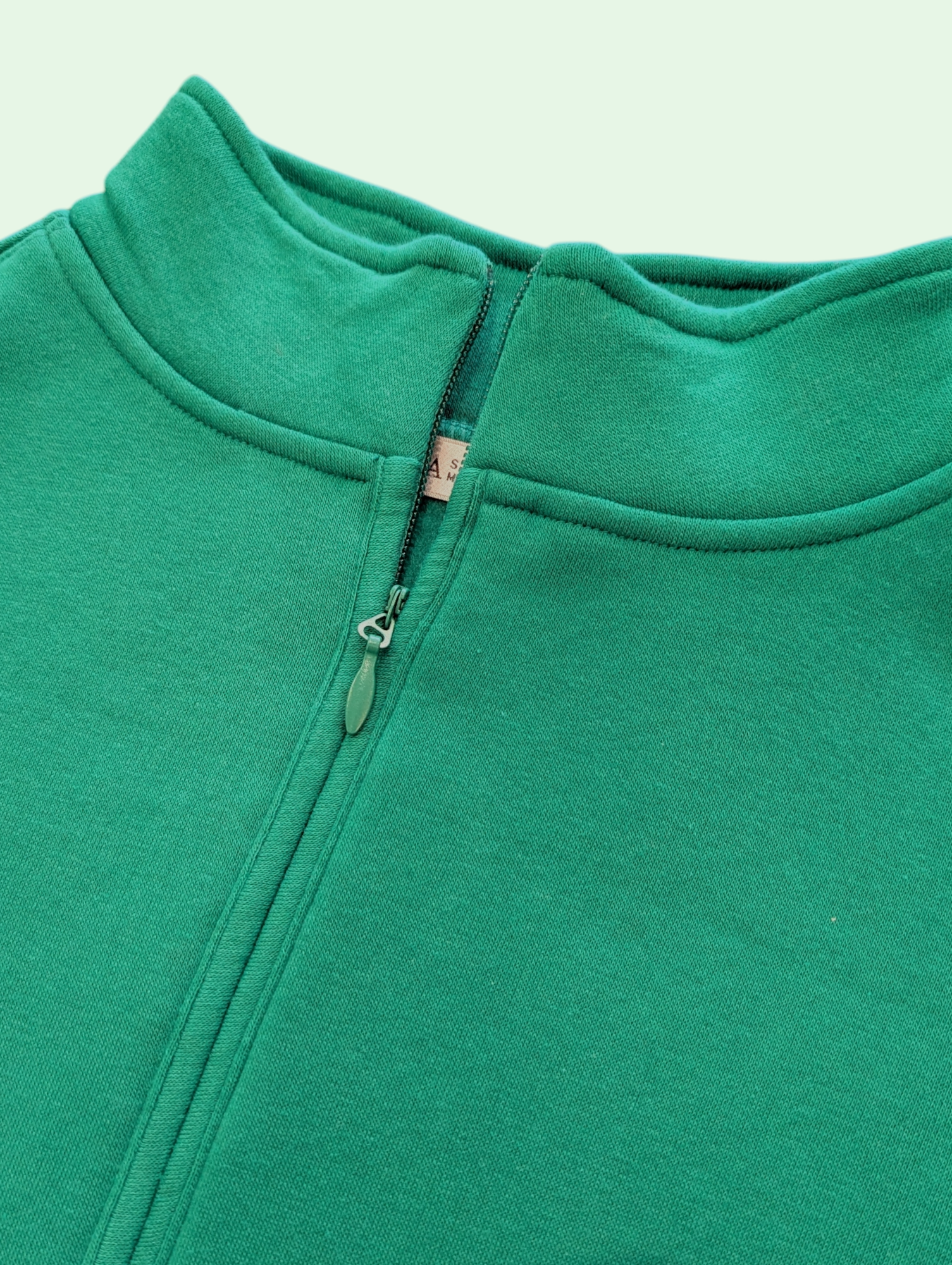 Close-up of a green fleece jacket with a zipper on a light green background