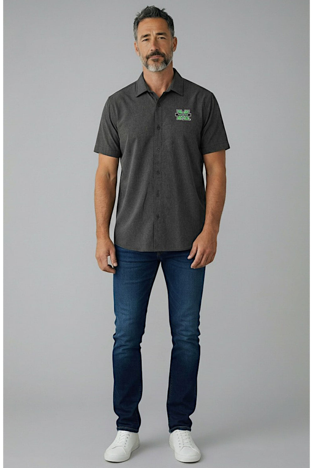 Man wearing a dark grey camp shirt with a logo and blue jeans on a gray background