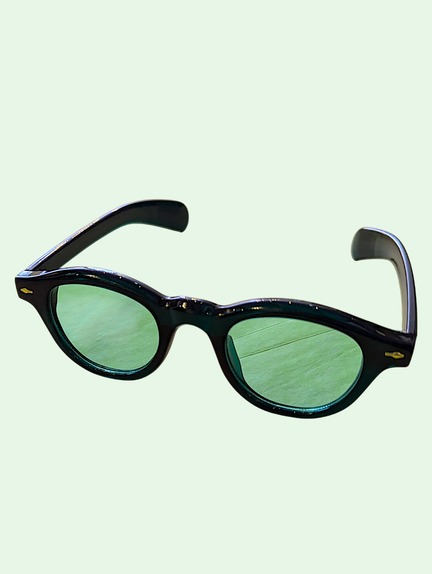 Sunglasses with green lenses and black frame on a light green background