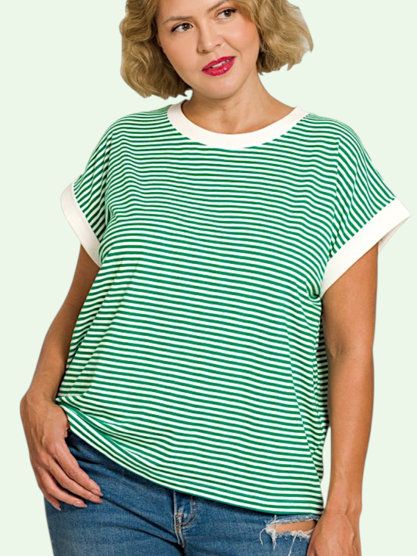 Woman wearing a green and white striped t-shirt with blue jeans on a light green background