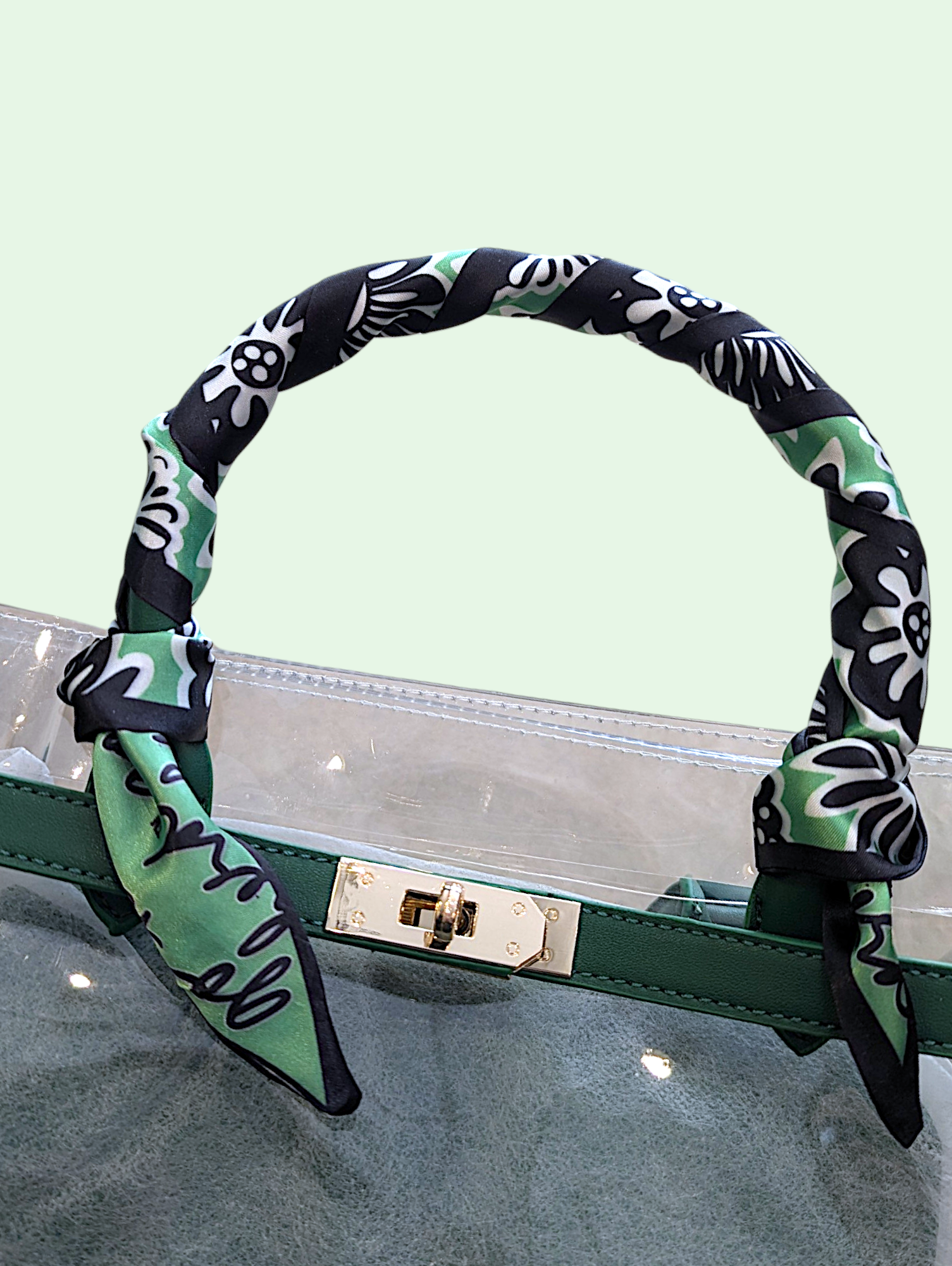 Green and black patterned scarf on a clear handbag with a light green background