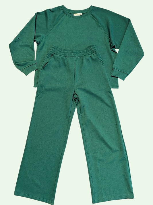 A two-piece loungewear set in a solid forest green color, featuring a long-sleeve raglan sweatshirt and matching wide-leg sweatpants, laid flat against a pale off-white background.