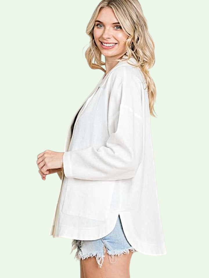 Woman wearing a white blazer over a black top with denim shorts on a light green background