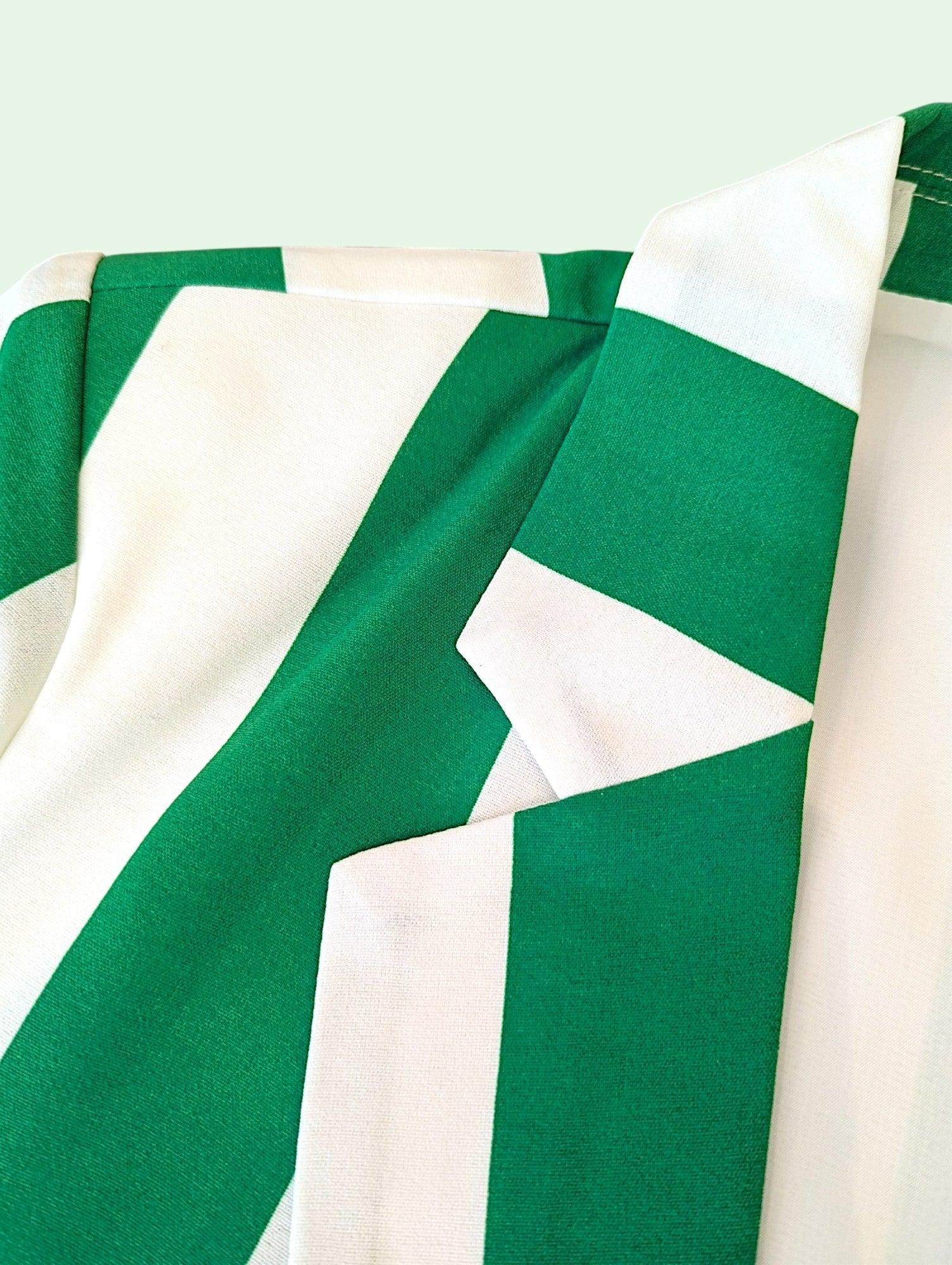 A close-up of a green and white striped garment, showing the collar and shoulder area with alternating wide green and white diagonal stripes.